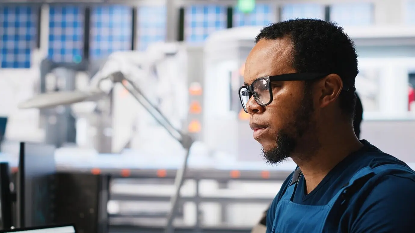 An African American engineer manages data from solar machinery on a desktop while working at a solar panel.